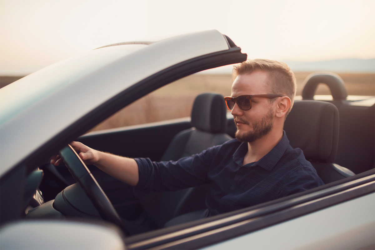 Man with sunglasses driving a convertible car on a sunny day