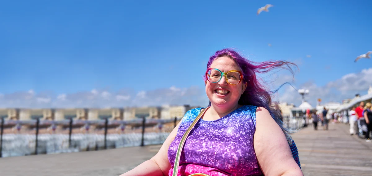 woman with purple hair and glasses smiling on the beach
