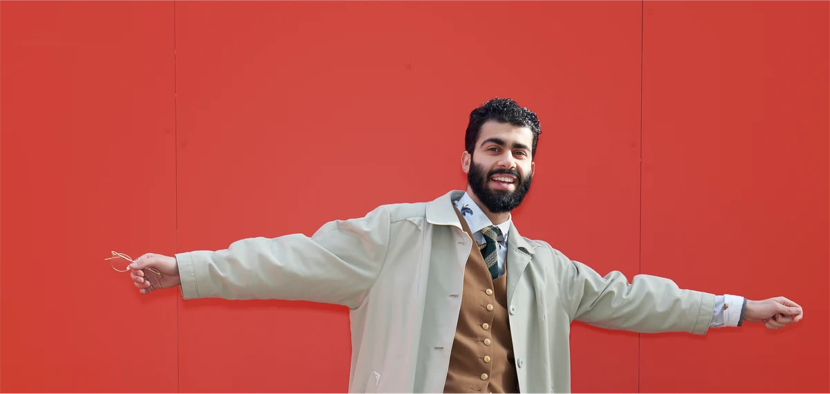 man with dark hair and beard standing in front of red wall