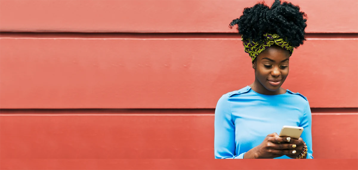 woman with afro hair and blue shirt looking at her phone