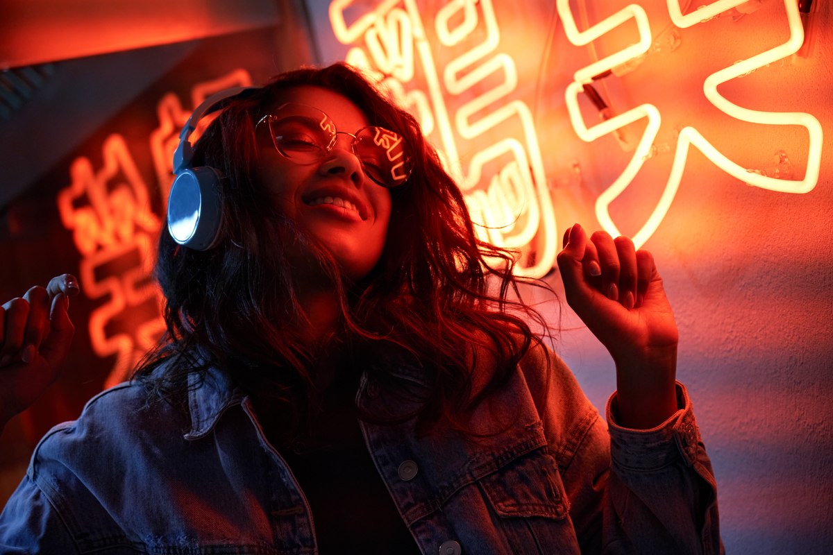 A woman wearing headphones dances to music under outdoor lights
