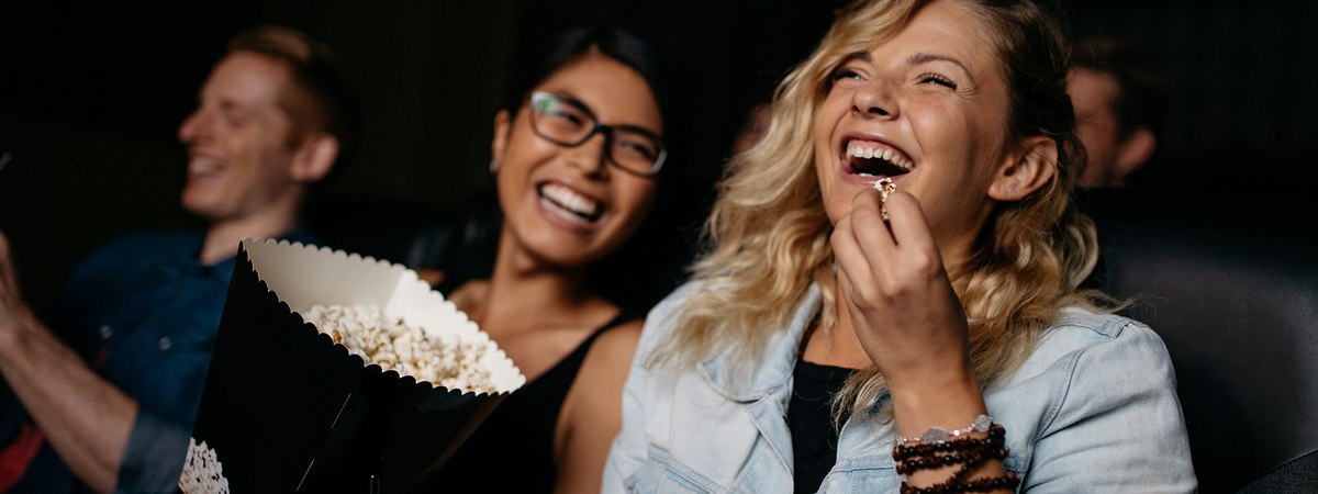 Leisure & Entertainment Hero Image featuring two women watching a movie at the cinema and eating popcorn