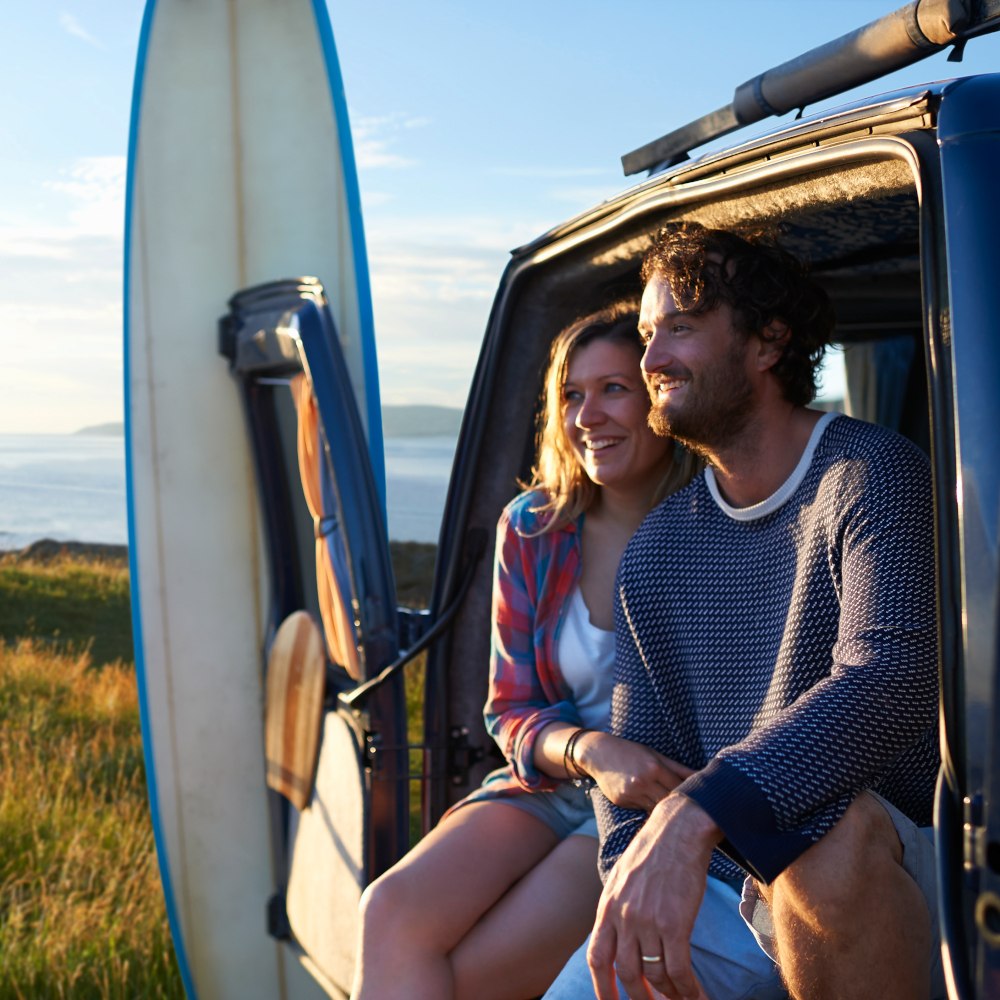 a traveling couple in a van with surfboards